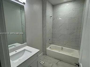 3304 11 Street W, #0, Lehigh Acres, FL 33971 Full bathroom featuring a white vanity with a rectangular sink, quartz countertop, wall-mounted mirror, and a tub enclosure with full-height stone-patterned tile surround