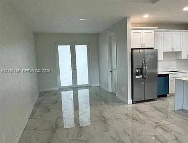 3304 11 Street W, #0, Lehigh Acres, FL 33971 Large-format polished tile flooring, white shaker-style cabinetry, stainless steel French-door refrigerator, and glass-paneled double doors