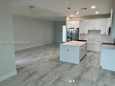 3304 11 Street W, #0, Lehigh Acres, FL 33971 Kitchen featuring white cabinetry, center island with stone-finish countertop, stainless steel refrigerator, and large-format tile flooring