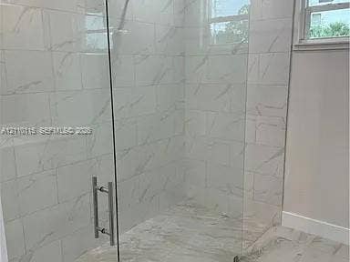3304 11 Street W, #0, Lehigh Acres, FL 33971 Walk-in shower featuring floor-to-ceiling large-format tile with veining, frameless glass enclosure, metallic hardware, and matching tile flooring