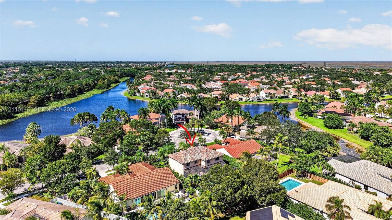 Aerial perspective of property featuring a multi-story residence with a tile roof, situated in a community with expansive water frontage and mature landscaping