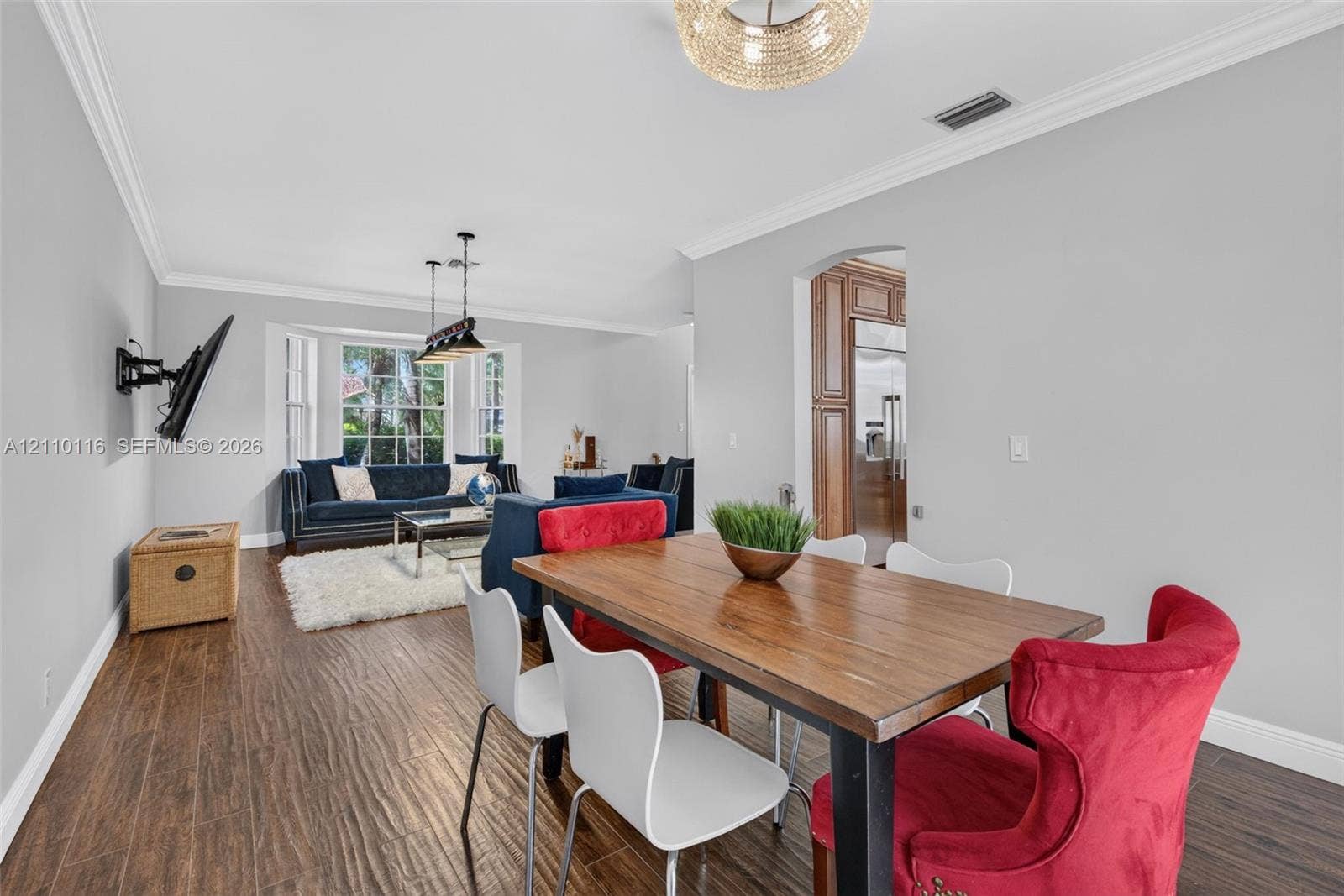 Open-concept area featuring wood-finish flooring, crown molding, a bay window, and a decorative chandelier