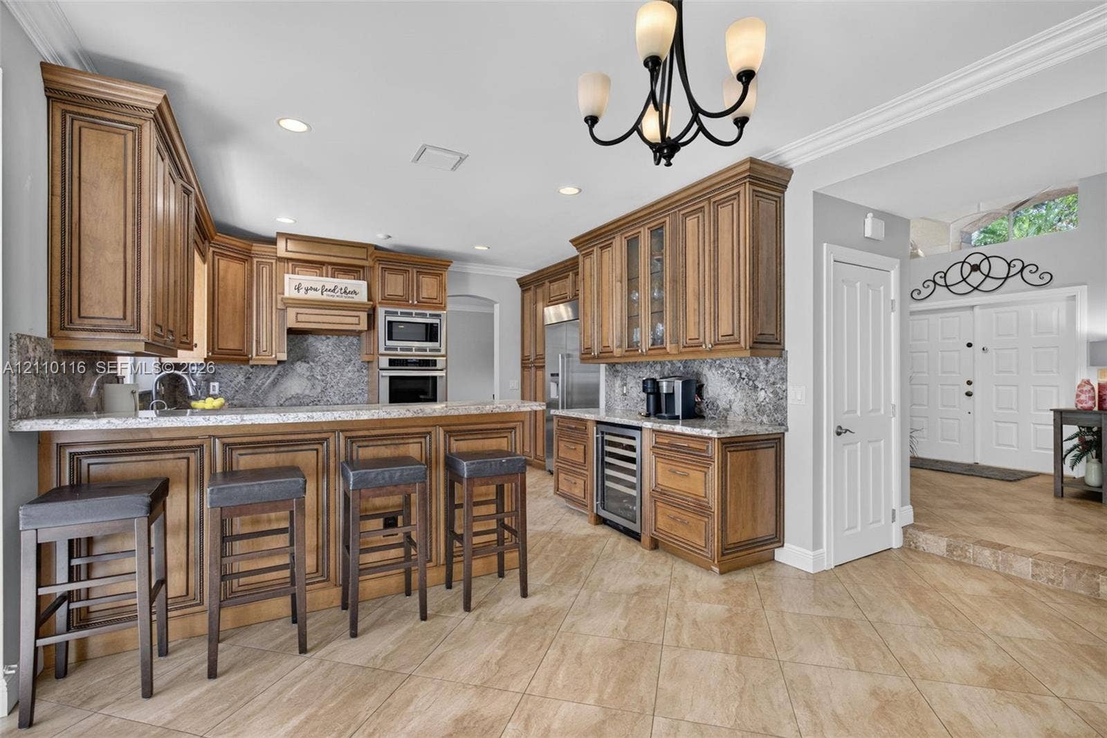 Kitchen featuring custom raised-panel wood cabinetry, stone countertops, integrated beverage refrigerator, recessed lighting, and a multi-arm chandelier