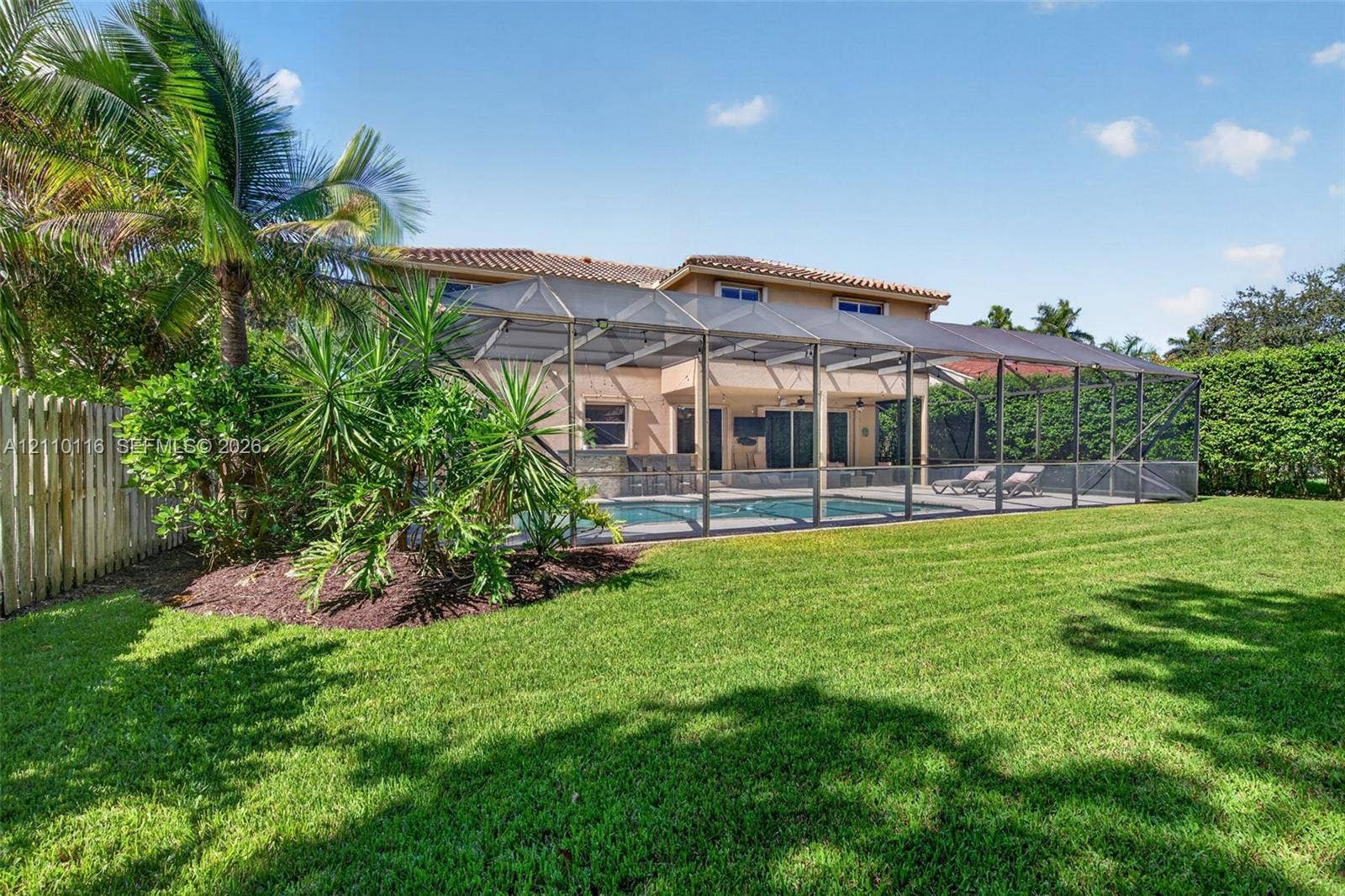Rear exterior featuring a screened-in swimming pool enclosure, stucco siding, a tiled roof, and a manicured lawn