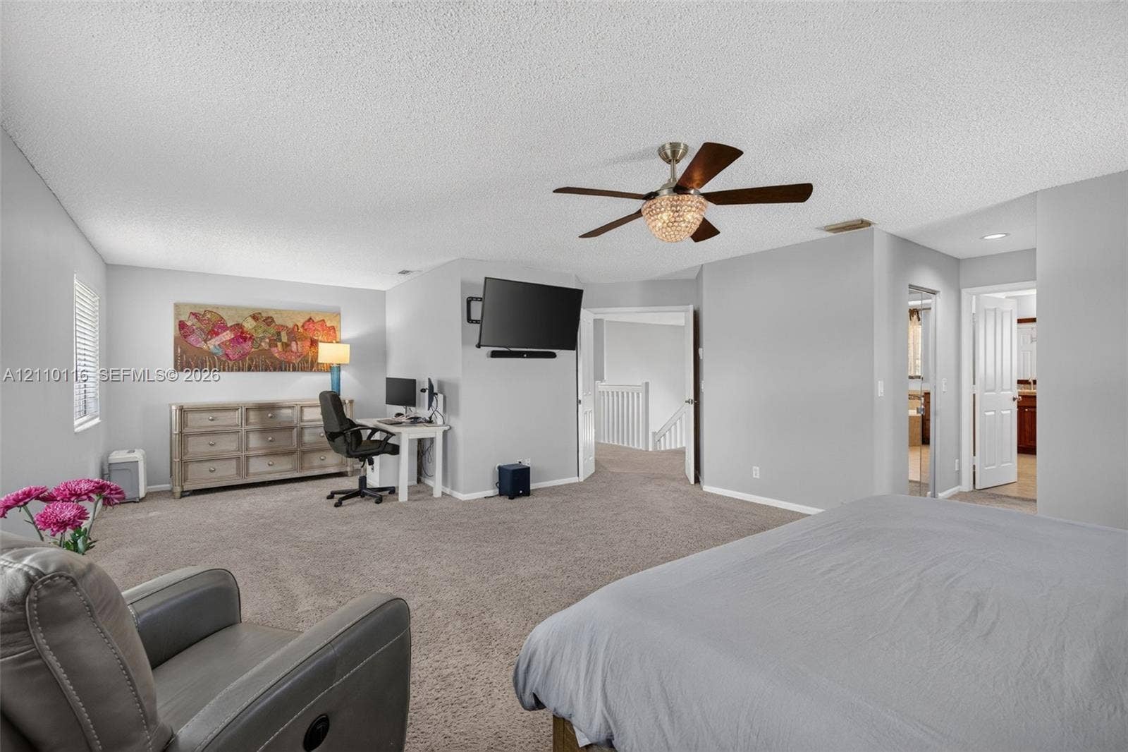 Spacious room featuring neutral carpeting, a central ceiling fan with an integrated crystal-style light fixture, and white interior doors