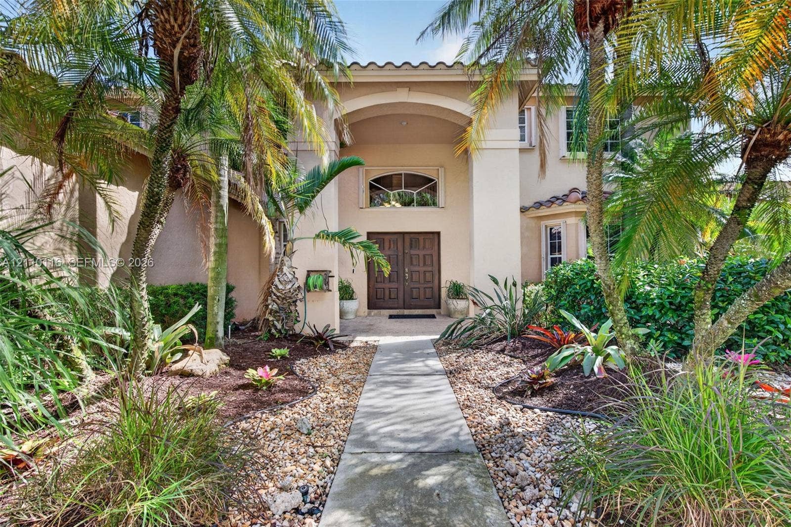 Stucco exterior featuring an arched entryway, double wood doors, arched transom window, and a tile roof