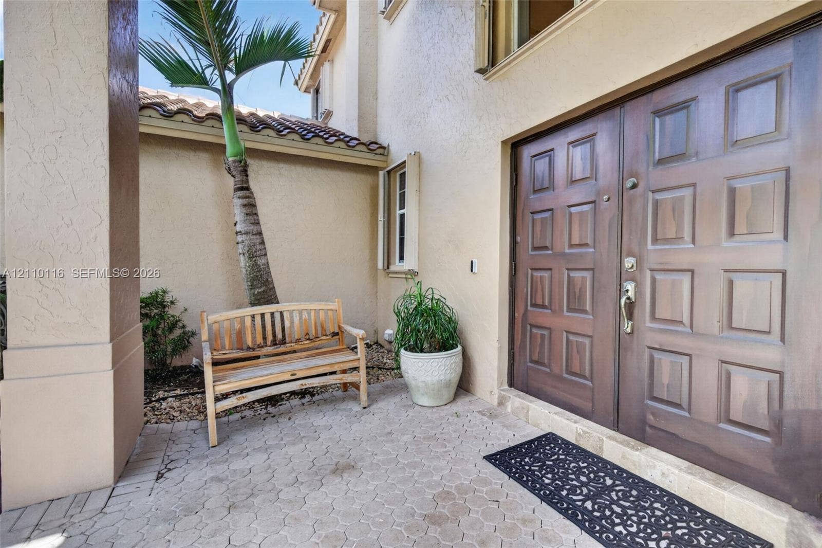 Stucco exterior entrance featuring a double-door entry with raised panel detailing, concrete paver flooring, and a tiled roofline