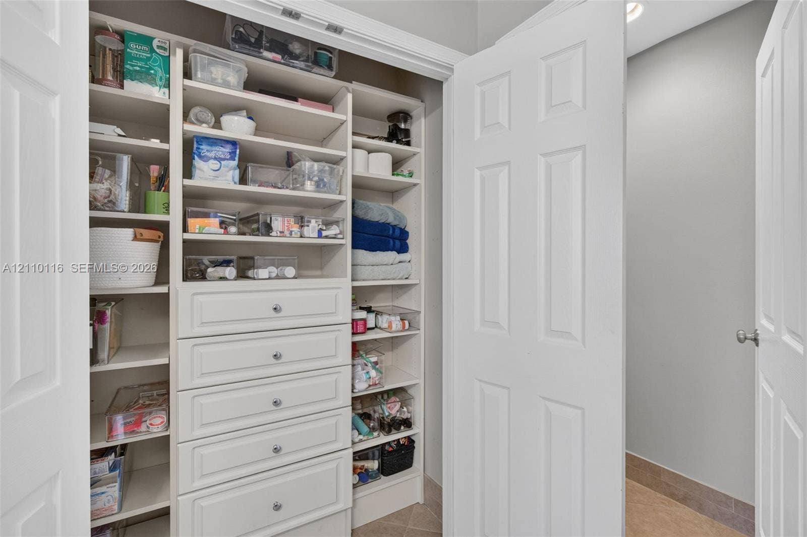 Linen closet featuring white built-in shelving, integrated drawers with metallic hardware, and double-door entry