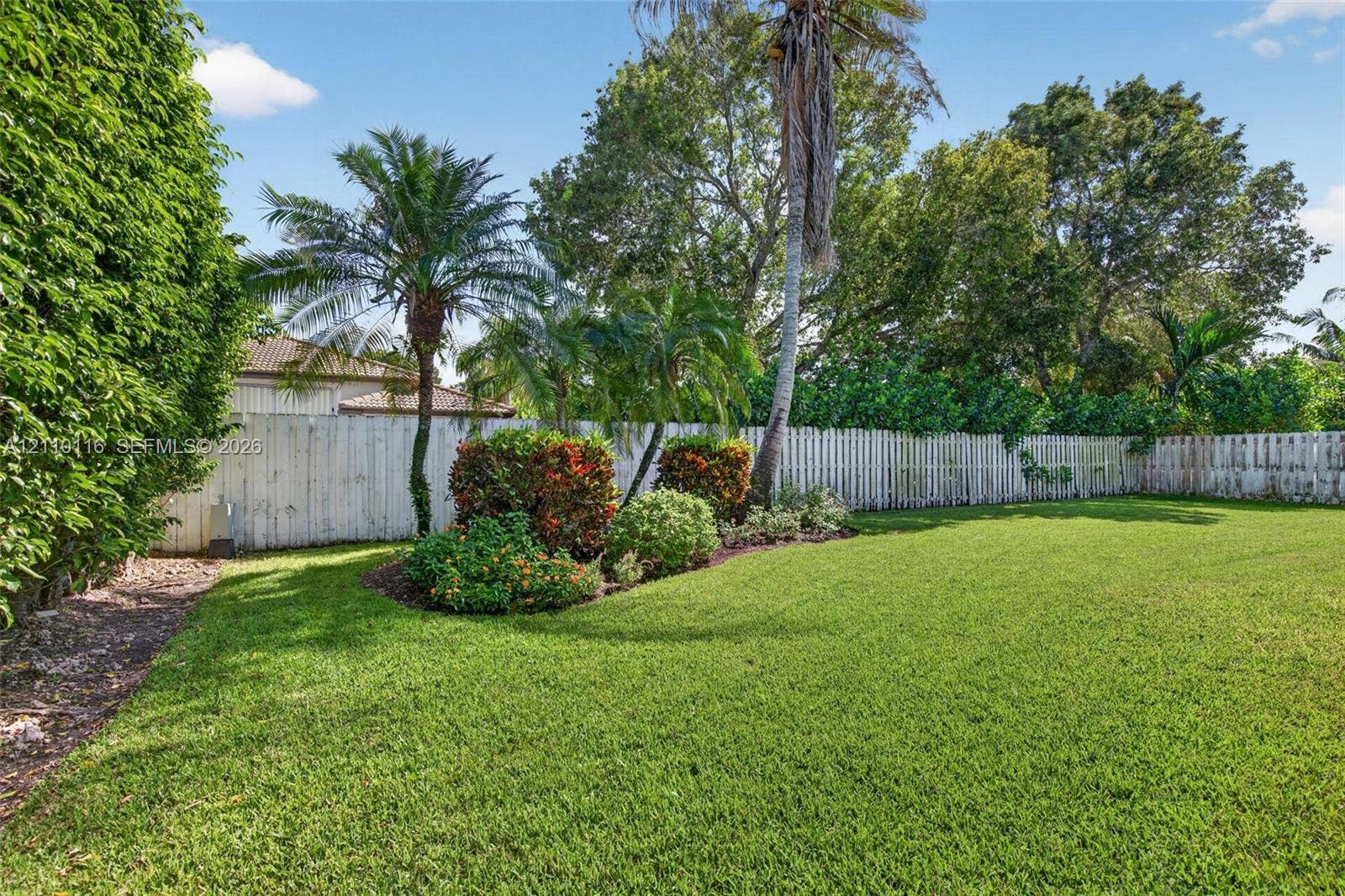 Expansive lawn featuring perimeter wood fencing, mature palm trees, and established shrubbery