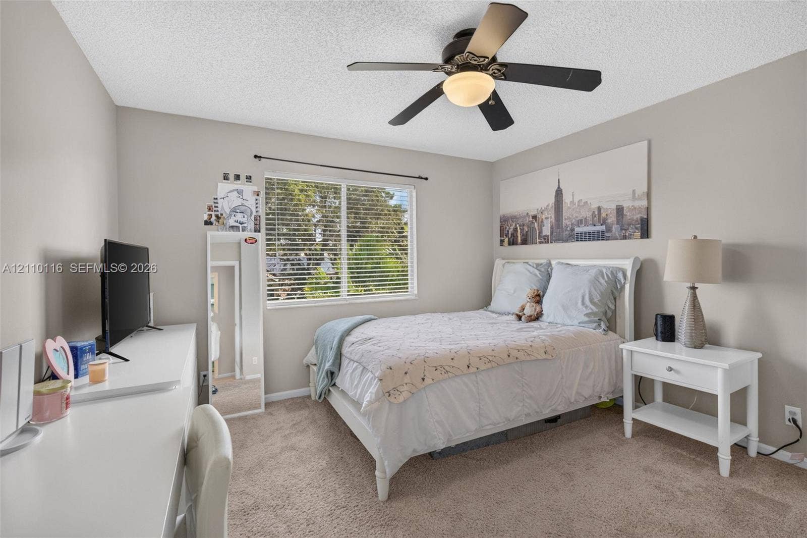 Neutral-toned room featuring wall-to-wall carpeting, a multi-blade ceiling fan with an integrated light fixture, and a window with a curtain rod