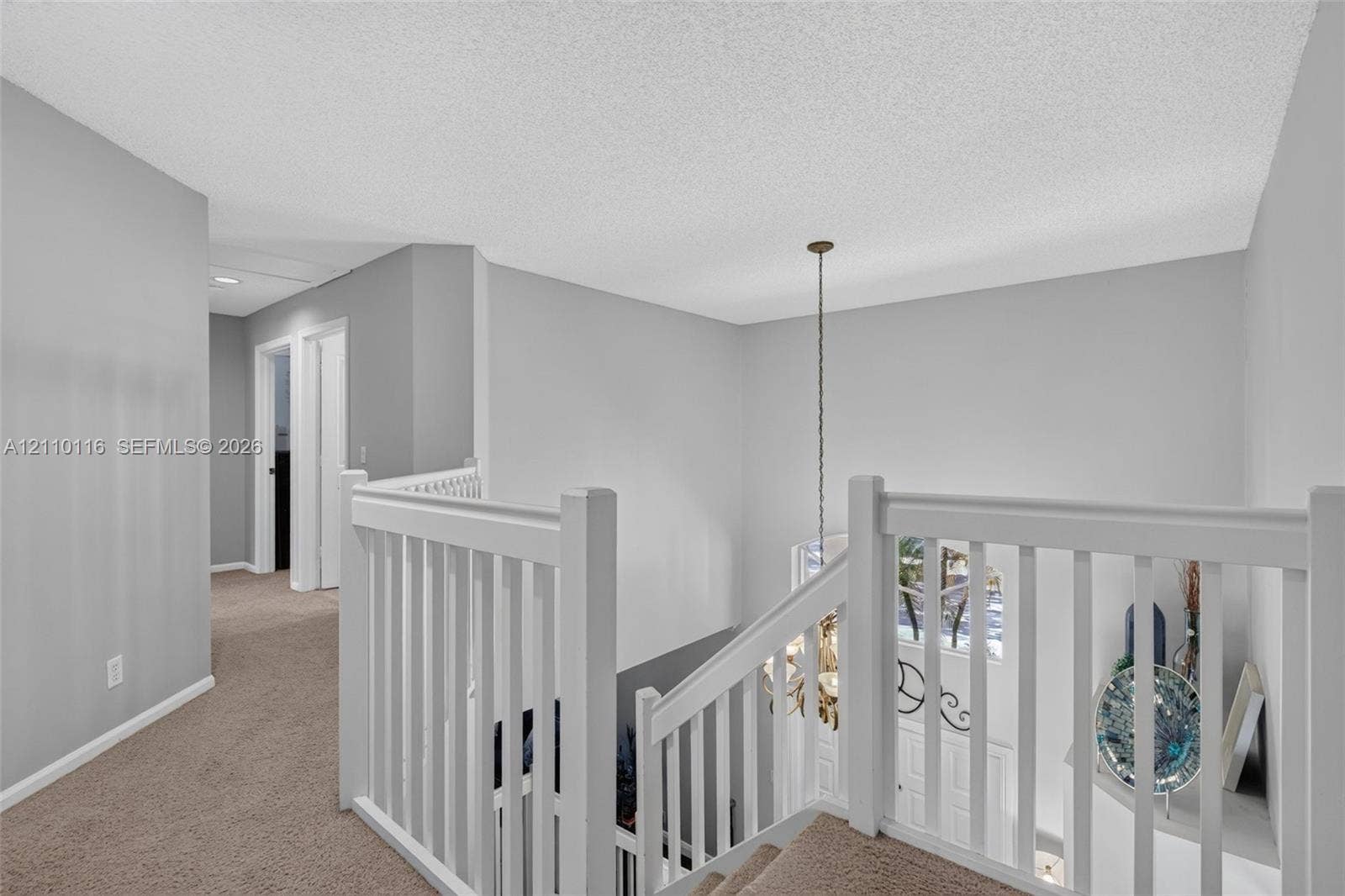 Landing area featuring neutral carpeting, white wooden balustrade, and a multi-light hanging chandelier