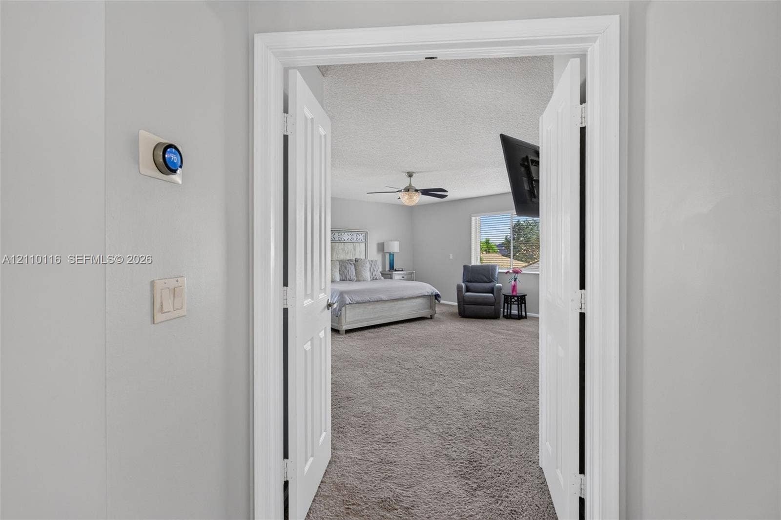 Double door entrance featuring wall-mounted smart thermostat, carpeted flooring, ceiling fan with integrated lighting, and dual-pane window
