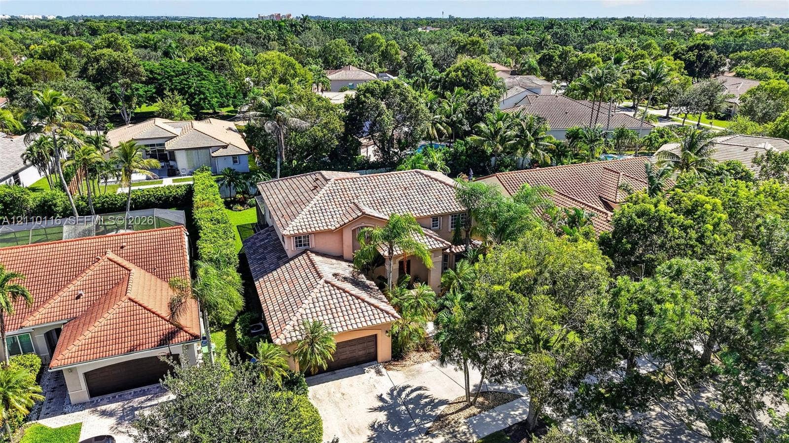 Two-story residence featuring a tile roof, stucco exterior, multi-car garage, and mature landscape