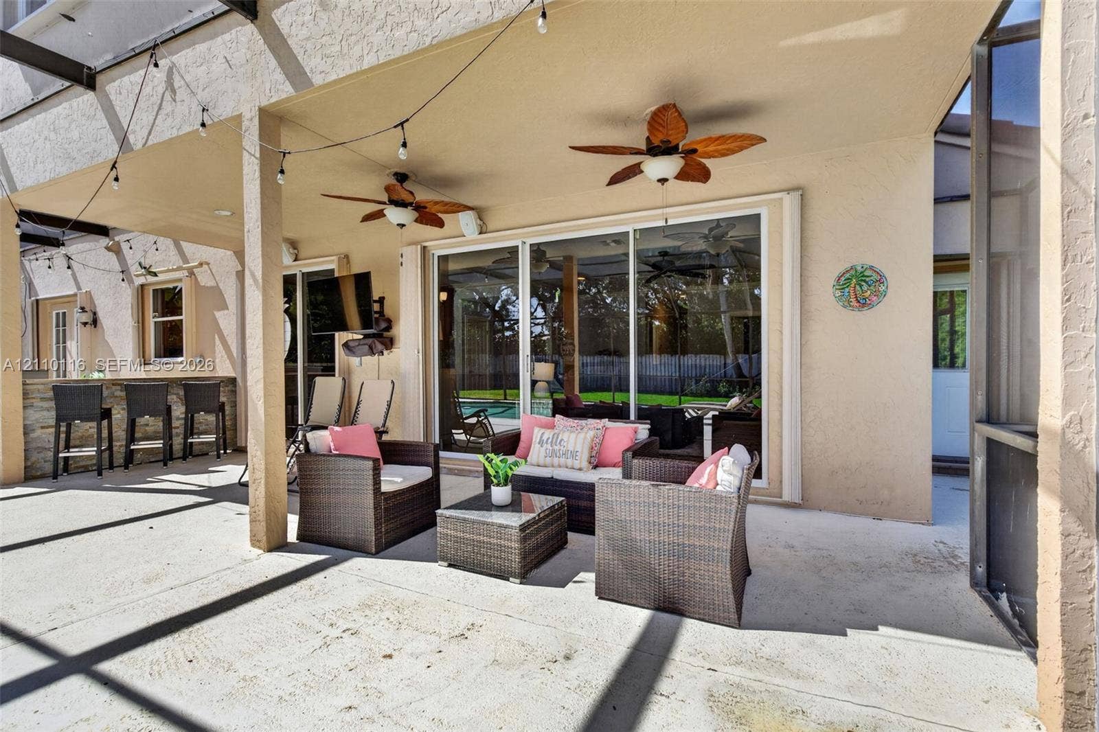 Covered outdoor living area featuring a concrete patio, stone-veneer wet bar, dual ceiling fans, and sliding glass entry doors