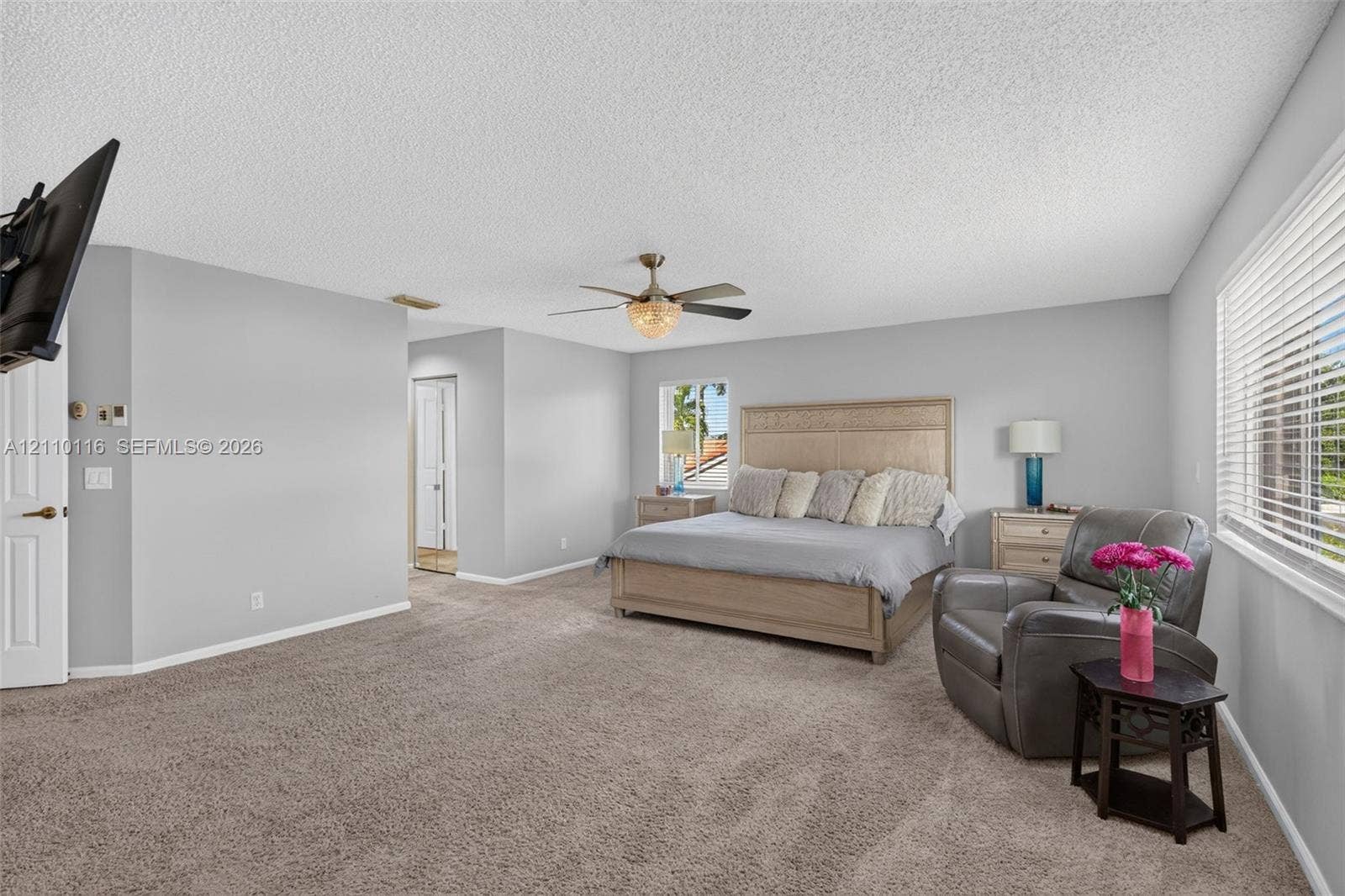 Spacious room featuring neutral carpeting, a central ceiling fan with integrated lighting, and horizontal blinds on the windows