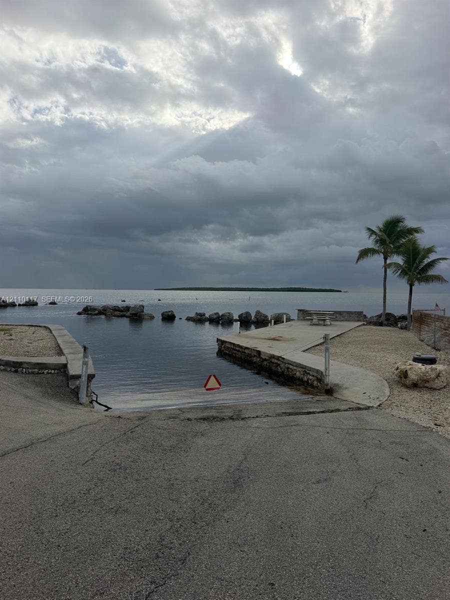 Private boat ramp featuring concrete surfacing, stone-lined bulkhead, and palm-lined waterfront access