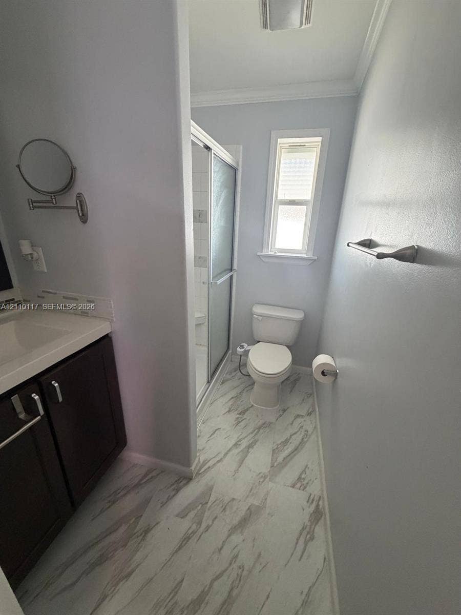Bathroom featuring dark wood-finish cabinetry, a white molded vanity countertop, shower enclosure with glass doors, and patterned tile flooring