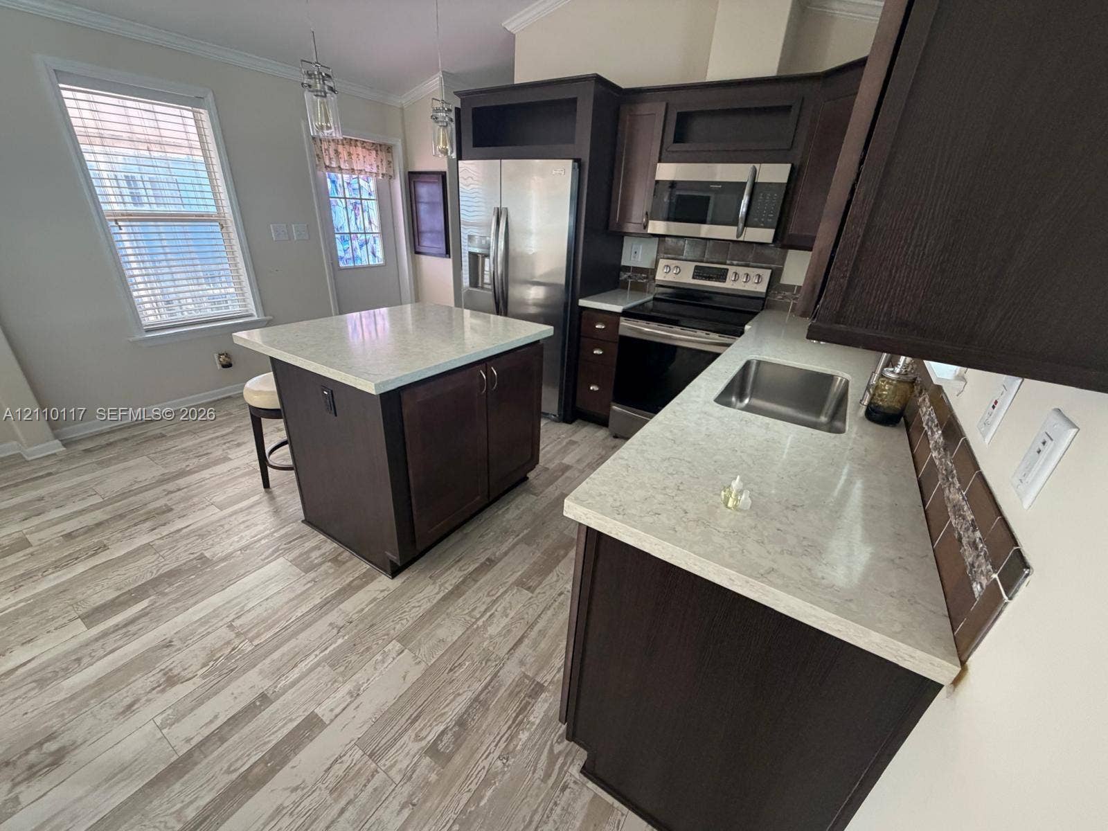 Kitchen featuring dark-finish cabinetry, an island with light-toned solid surface countertops, stainless steel appliances, and wood-finish flooring