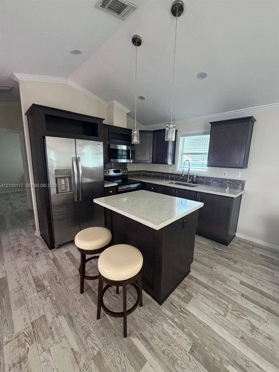 Kitchen featuring dark cabinetry, stone-finish countertops, stainless steel appliances, a center island, and wood-finish flooring