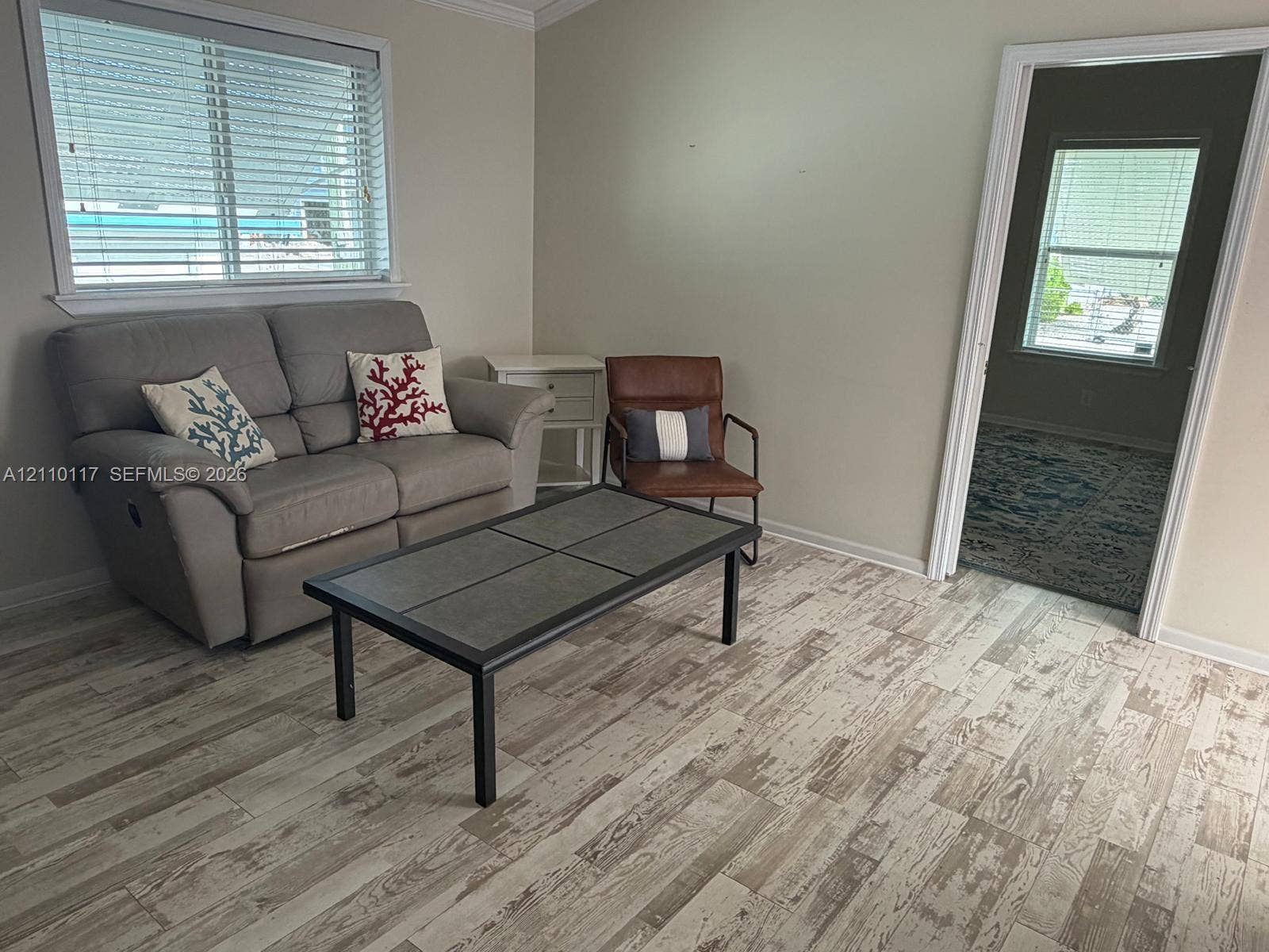 Wood-finish flooring, neutral wall tones, crown molding, and horizontal slat window blinds