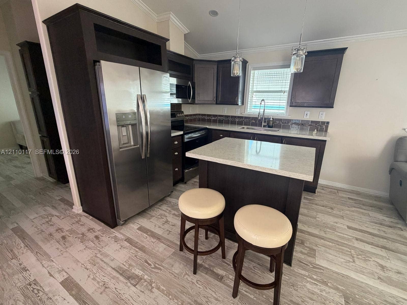 Kitchen featuring dark-finish cabinetry, a center island with a stone-composite countertop, wood-finish flooring, stainless steel appliances, and glass pendant lighting