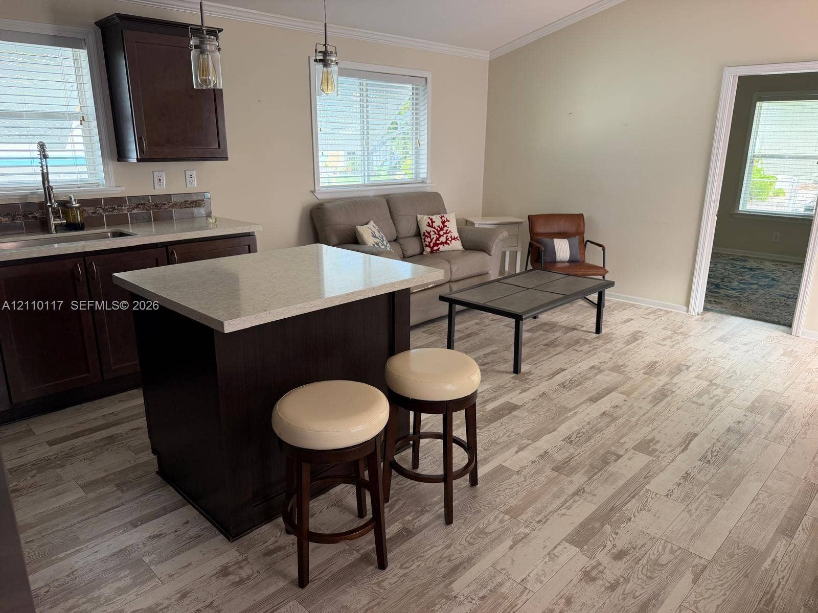 Kitchen featuring dark wood-finish cabinetry, stone-style countertops, an integrated island, neutral wood-finish flooring, and two glass-pendant light fixtures