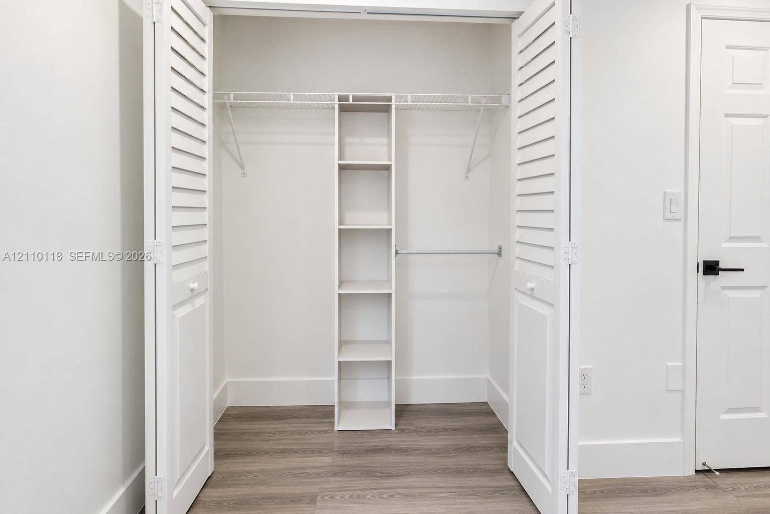 7991 SW 152nd Avenue, #701-7, Miami, Miami, FL 33193 Closet featuring white louvered bifold doors, integrated shelving unit, wire hanging racks, and wood-finish flooring