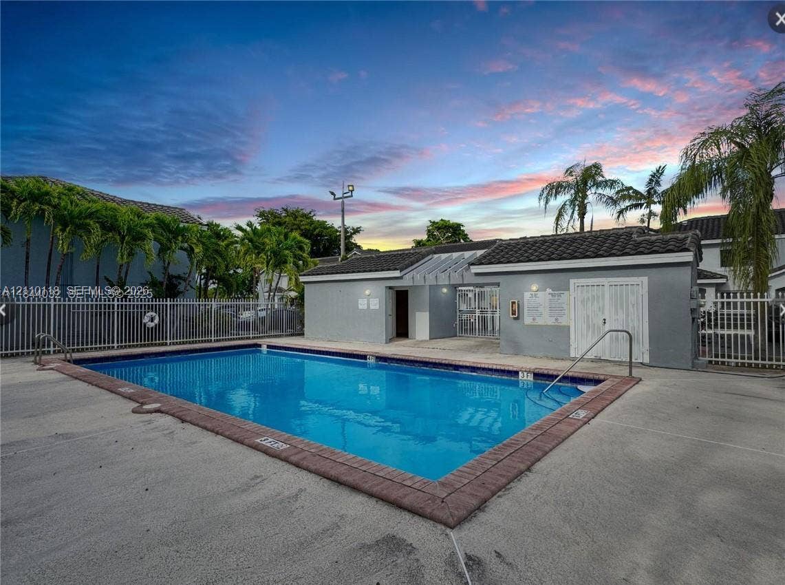 7991 SW 152nd Avenue, #701-7, Miami, Miami, FL 33193 Rectangular swimming pool featuring a brick paver border, concrete decking, metal perimeter fencing, and an attached auxiliary building with a tiled roof