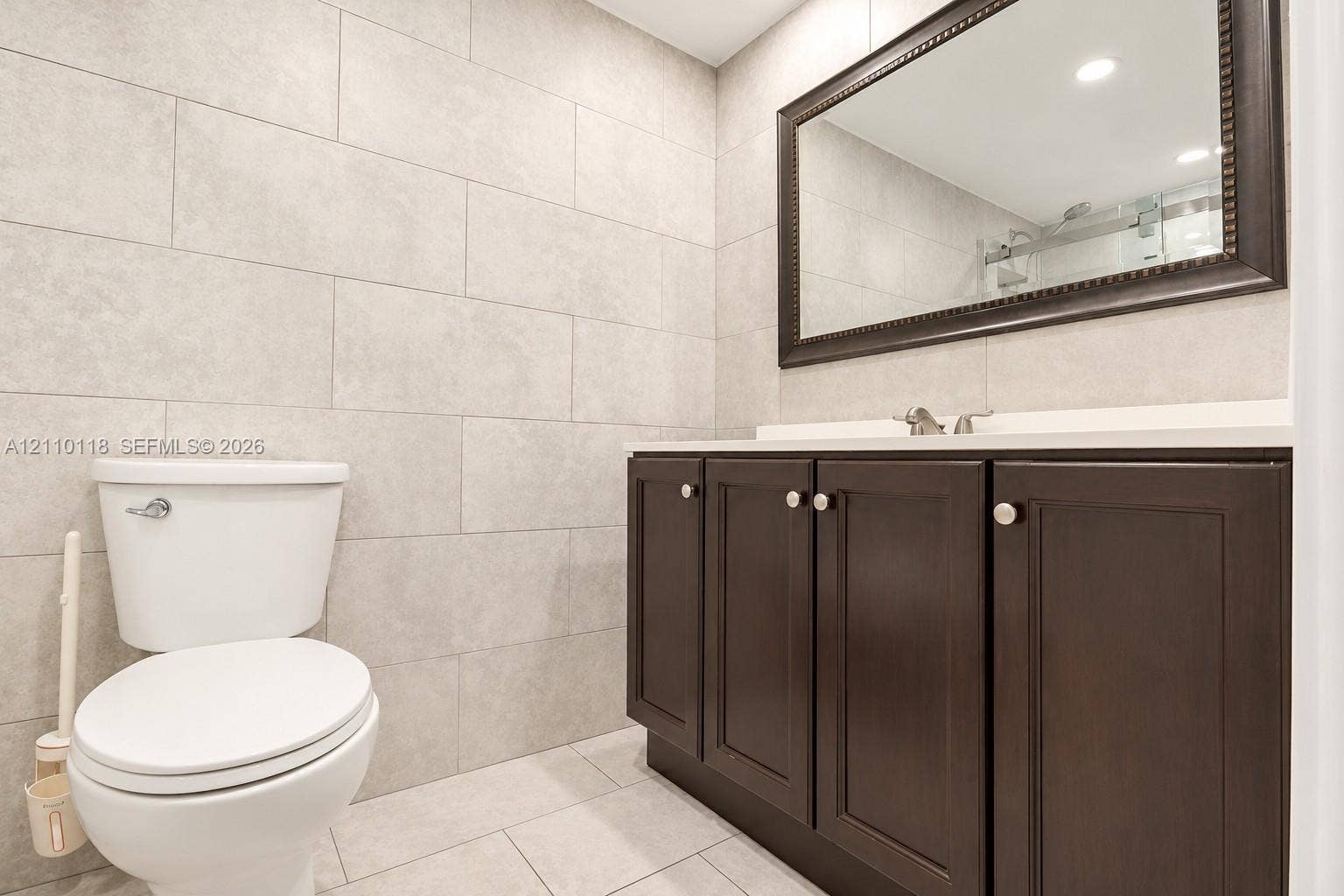 7991 SW 152nd Avenue, #701-7, Miami, Miami, FL 33193 Bathroom featuring large-format wall and floor tiling, dark wood-finish cabinetry, a solid surface countertop, and a framed mirror