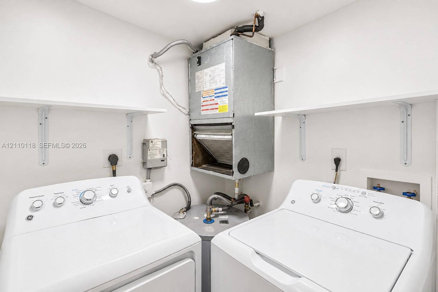 7991 SW 152nd Avenue, #701-7, Miami, Miami, FL 33193 Utility space featuring a wall-mounted air handler, a water heater, dual wall-mounted shelving units, and dedicated hookups for laundry appliances