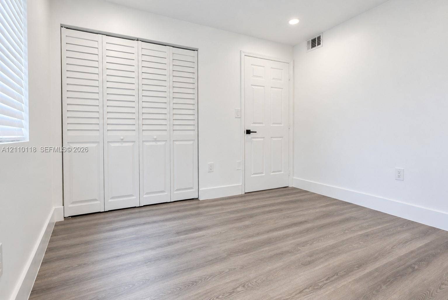 7991 SW 152nd Avenue, #701-7, Miami, Miami, FL 33193 Neutral interior featuring wood-finish flooring, white louvered closet doors, a six-panel door with matte black hardware, and recessed lighting