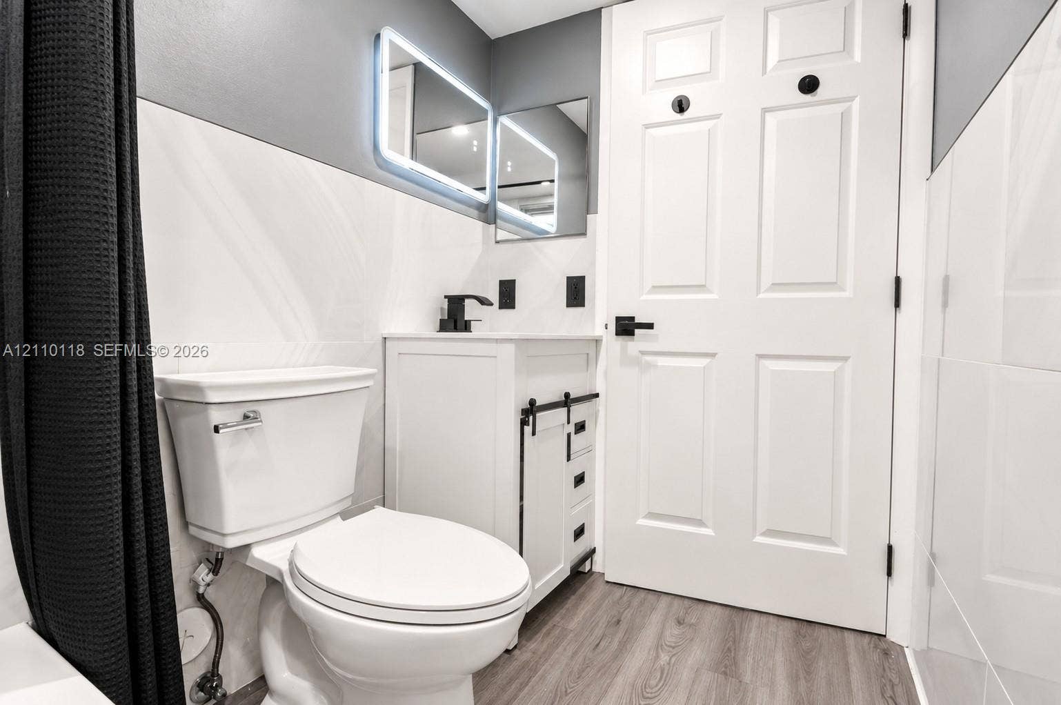 7991 SW 152nd Avenue, #701-7, Miami, Miami, FL 33193 Bathroom featuring a white vanity cabinet with black sliding barn-door hardware, an integrated sink with a matte black faucet, a rectangular LED-backlit mirror, and wood-finish flooring