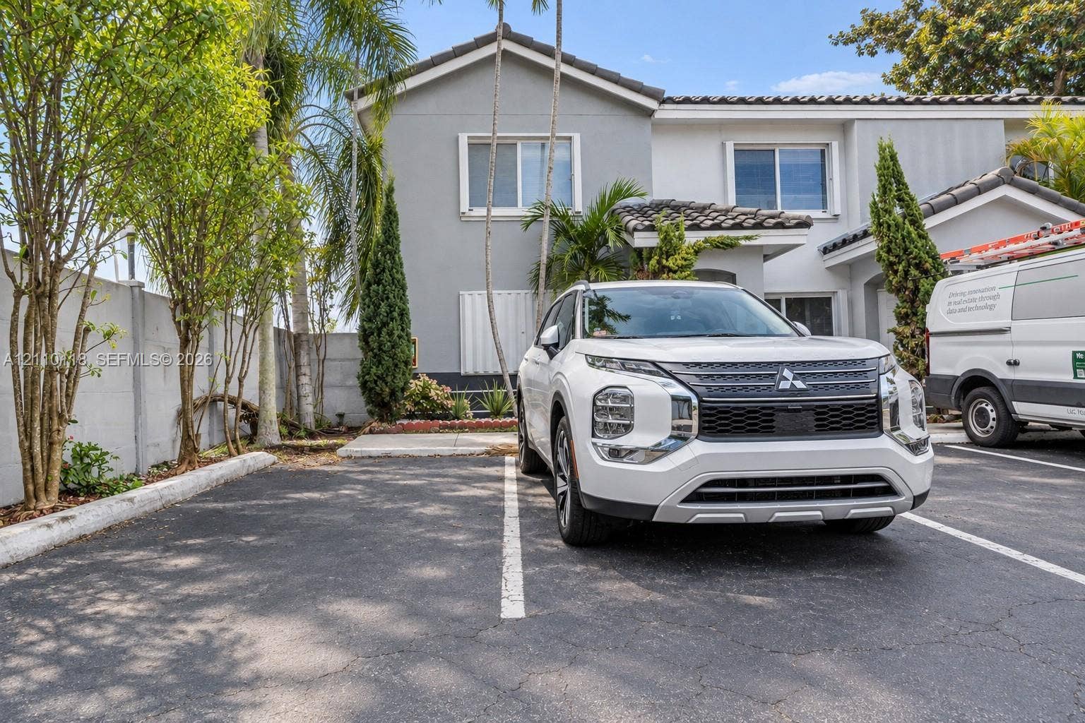 7991 SW 152nd Avenue, #701-7, Miami, Miami, FL 33193 Exterior view of a multi-level structure featuring a neutral-toned stucco facade, tiled roofline, dedicated asphalt parking spaces, and perimeter concrete block wall