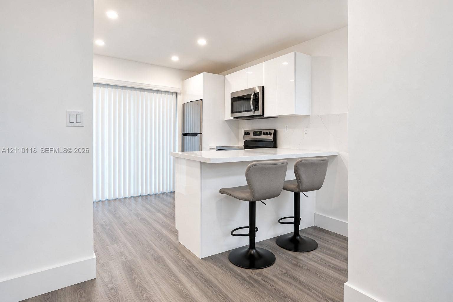 7991 SW 152nd Avenue, #701-7, Miami, Miami, FL 33193 Kitchen featuring high-gloss white cabinetry, white stone-finish countertop with breakfast bar seating, stainless steel appliances, and wood-finish flooring