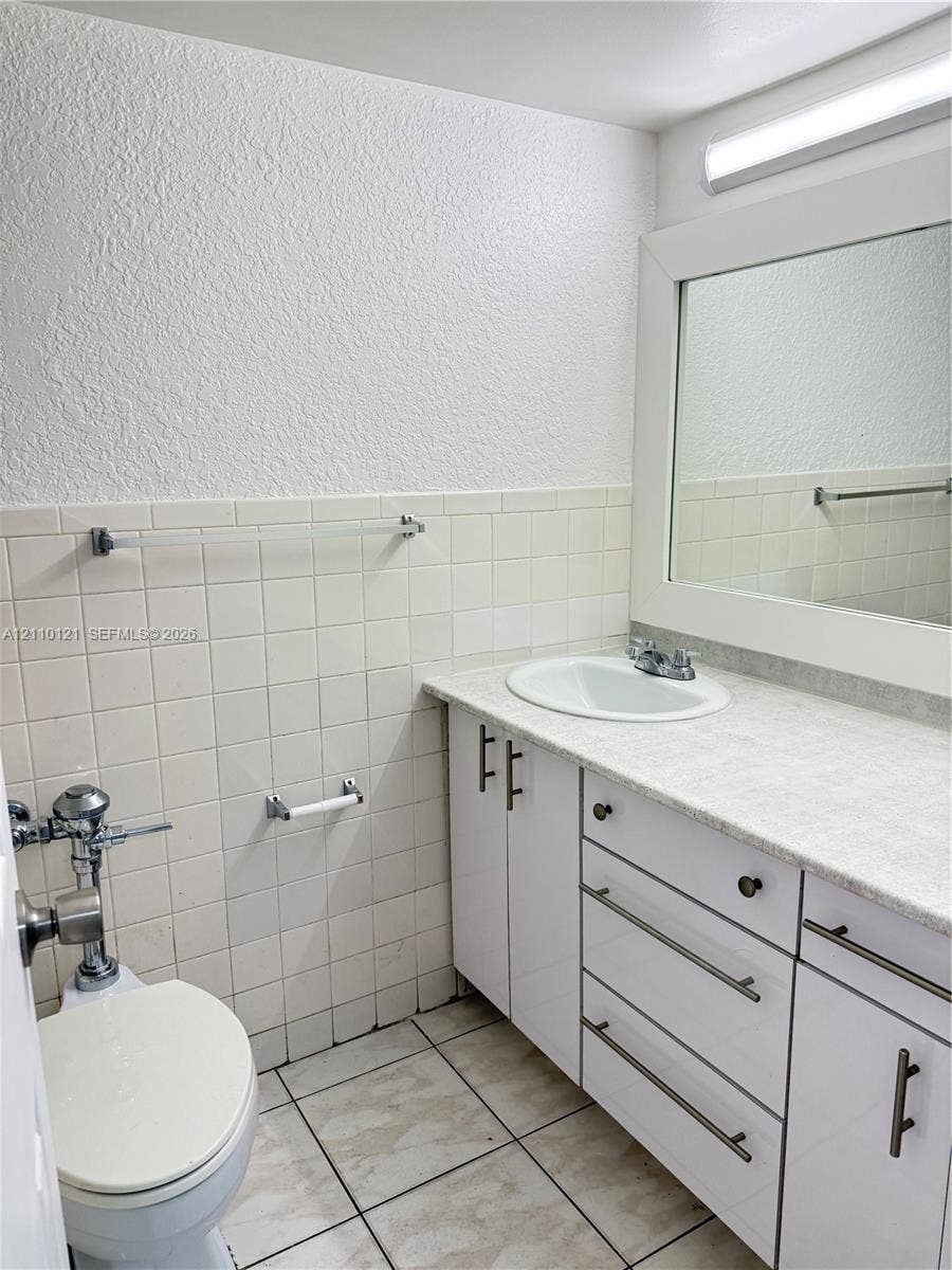 Bathroom featuring a white vanity cabinet with metallic hardware, integrated countertop with a recessed basin, framed wall mirror, and ceramic tile wall accents