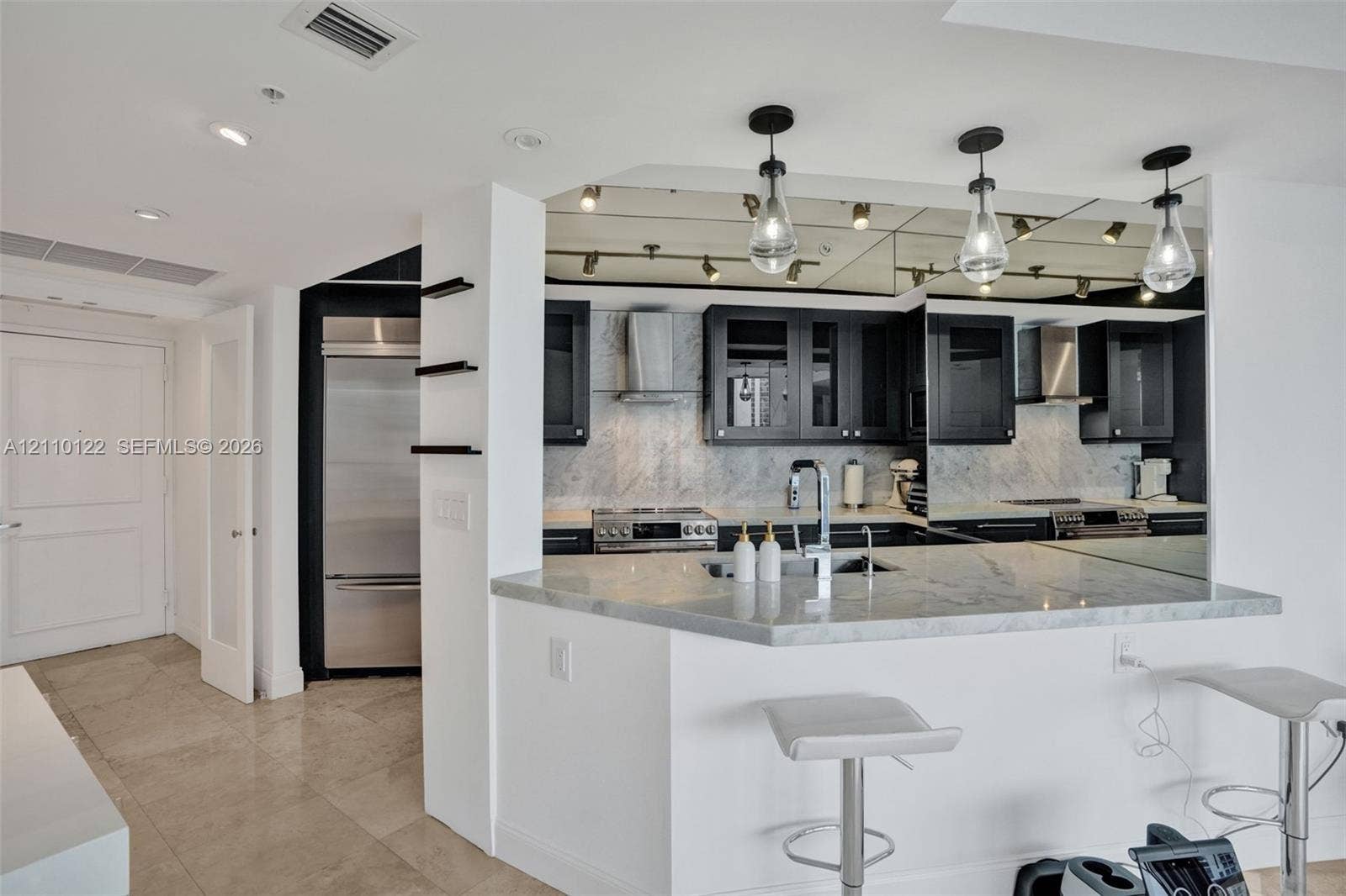 333 Las Olas Way, #2708, Fort Lauderdale, FL 33301 Kitchen featuring stone-surfaced countertops, custom cabinetry with glass-front accents, stainless steel appliances, mirrored backsplash, and pendant lighting