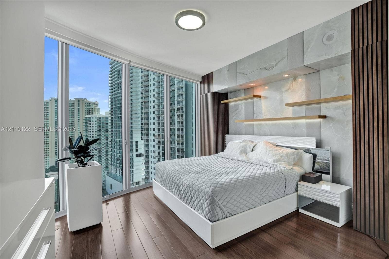 333 Las Olas Way, #2708, Fort Lauderdale, FL 33301 Floor-to-ceiling windows, wood-finish flooring, stone-clad accent wall, custom built-in shelving, and vertical wood-slat wall paneling