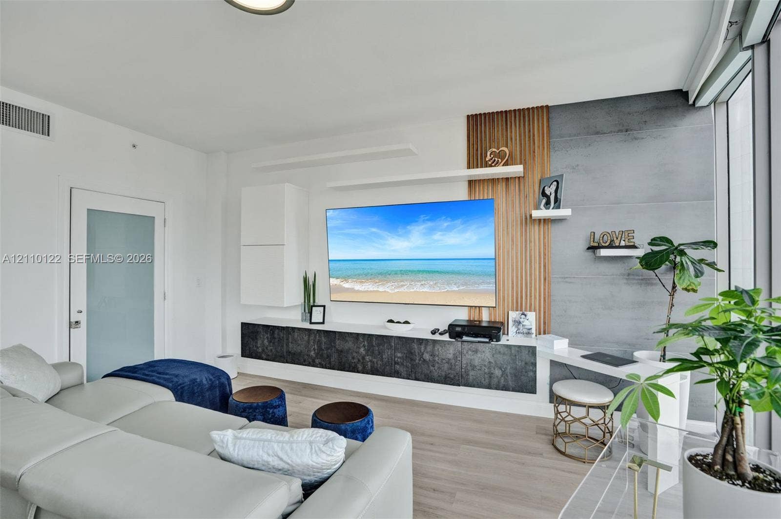 333 Las Olas Way, #2708, Fort Lauderdale, FL 33301 Custom built-in media console featuring vertical wood slat paneling, dark textured cabinetry, concrete-finish wall detail, floating display shelves, and integrated desk workspace