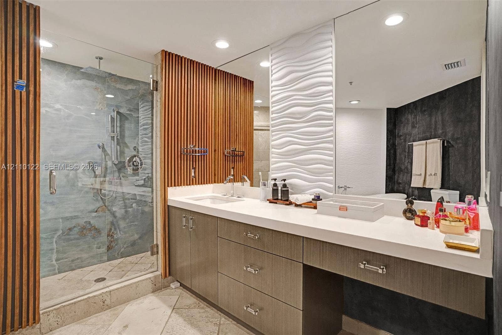 333 Las Olas Way, #2708, Fort Lauderdale, FL 33301 Bathroom featuring a glass-enclosed shower with stone-tile surround, wall-mounted wood-slat paneling, a white dimensional wave-pattern wall accent, a dual-sink vanity with solid-surface countertop, and recessed lighting