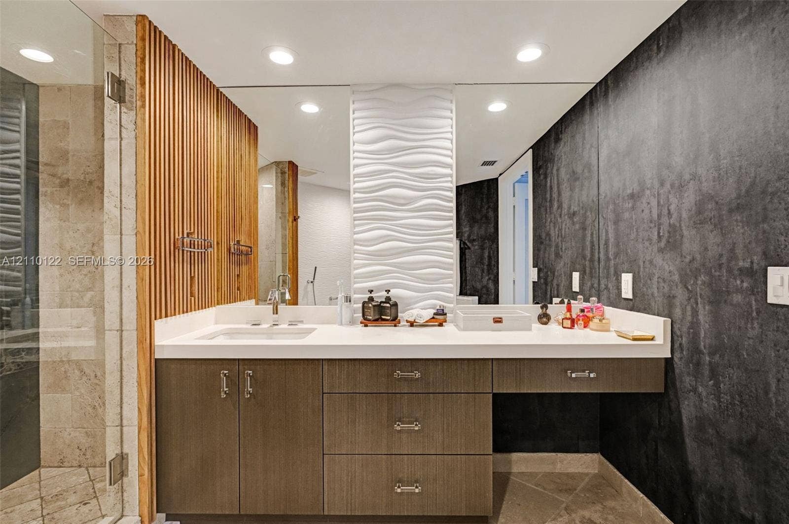 333 Las Olas Way, #2708, Fort Lauderdale, FL 33301 Custom vanity with stone countertop and integrated sink, vertical wood-slat accent wall, 3D wave-pattern wall tile, recessed ceiling lighting, and floor-to-ceiling mirror