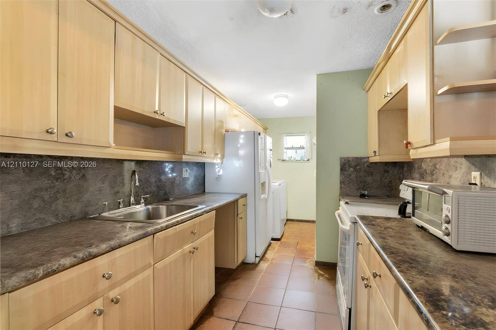 10164 SW 52nd Street, Cooper City, FL 33328 Kitchen featuring wood-finish cabinetry, stone-texture laminate countertops, dark stone-style backsplash, integrated stainless steel sink with metal faucet, and tile flooring