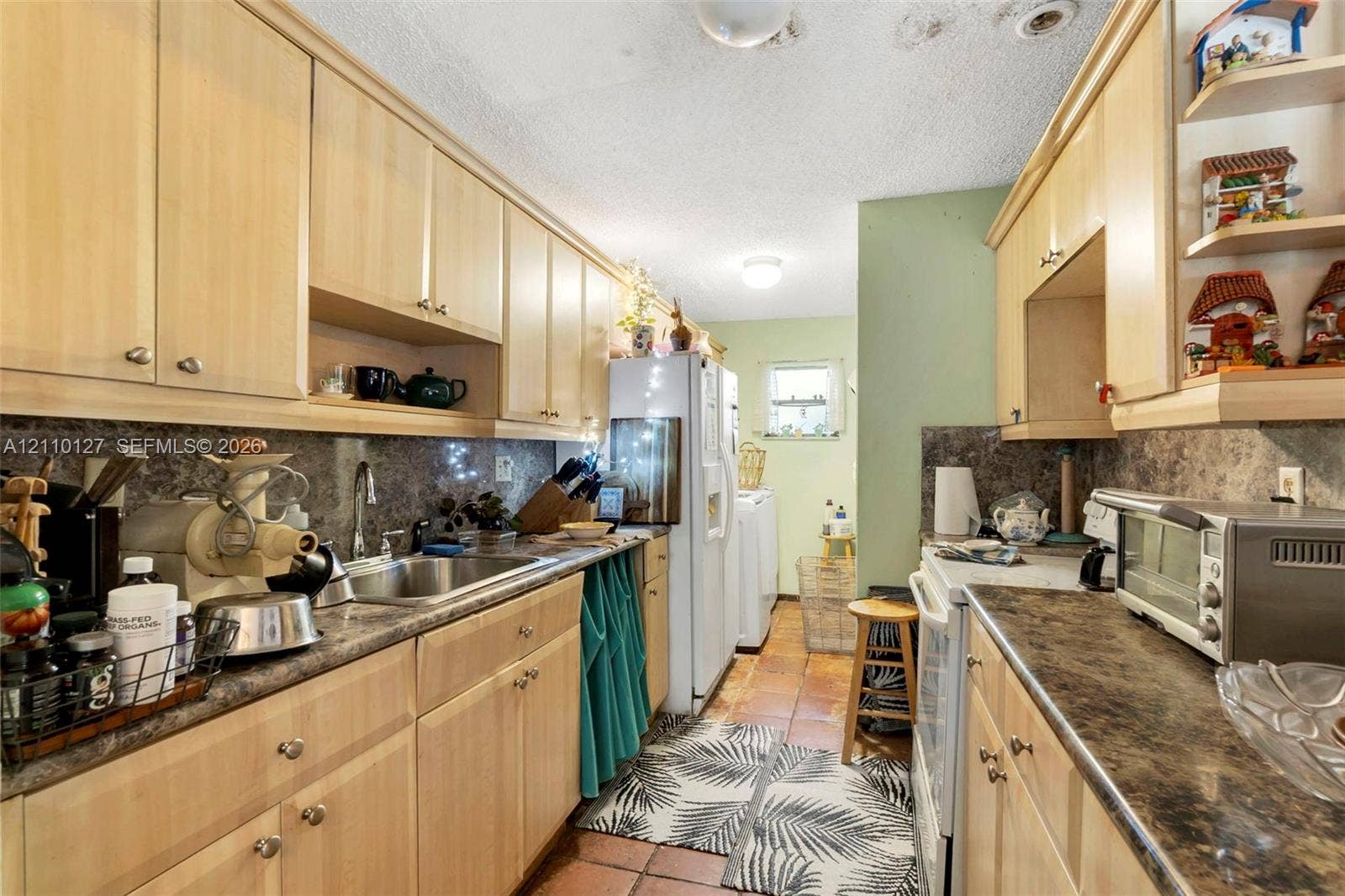 10164 SW 52nd Street, Cooper City, FL 33328 Galley kitchen featuring light wood-finish cabinetry, stone-texture laminate countertops, stainless steel sink with metal faucet, and terra-cotta tile flooring
