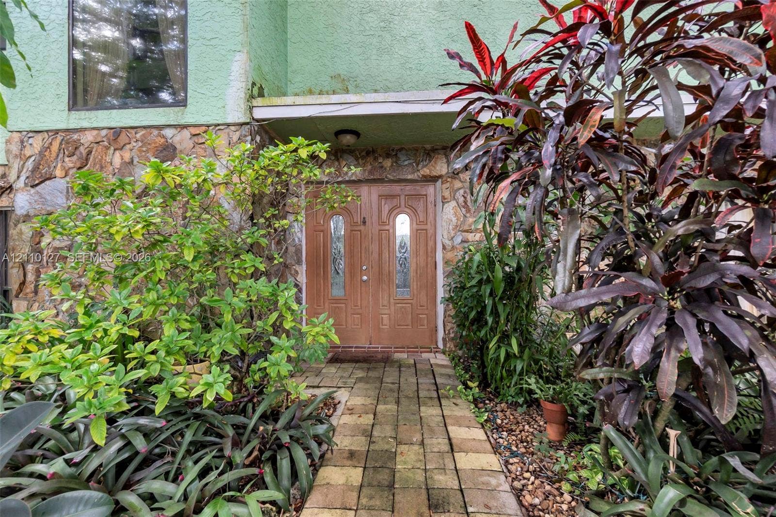 10164 SW 52nd Street, Cooper City, FL 33328 Exterior entrance featuring double doors with decorative glass inserts, natural stone masonry facade, stucco detailing, and a brick paver walkway