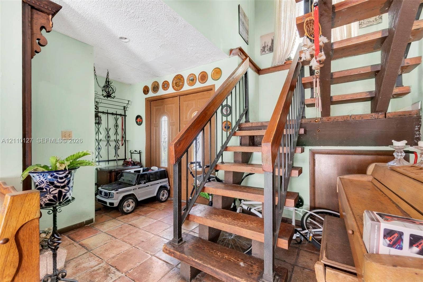 10164 SW 52nd Street, Cooper City, FL 33328 Foyer entry featuring dual wood doors with glass inserts, terra cotta tile flooring, and an open-riser staircase with wood treads and metal balusters