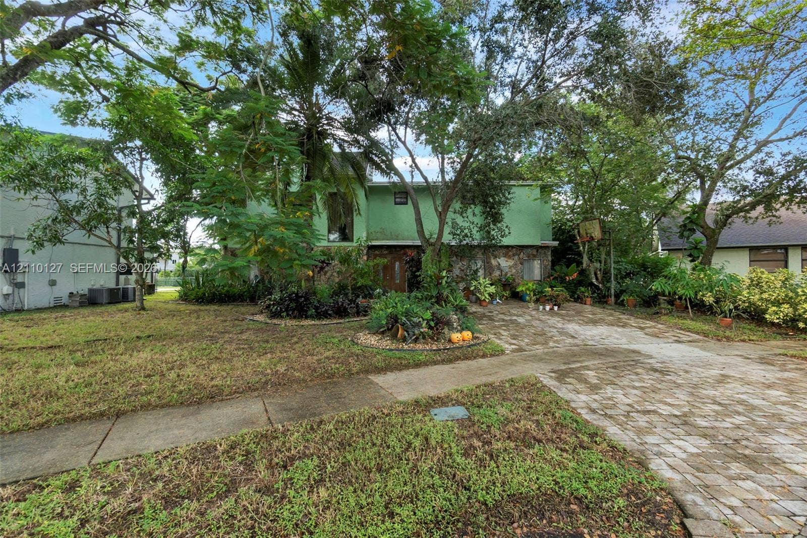 10164 SW 52nd Street, Cooper City, FL 33328 Two-story residence featuring a stone-accented facade, paved driveway, mature shade trees, and integrated landscaping