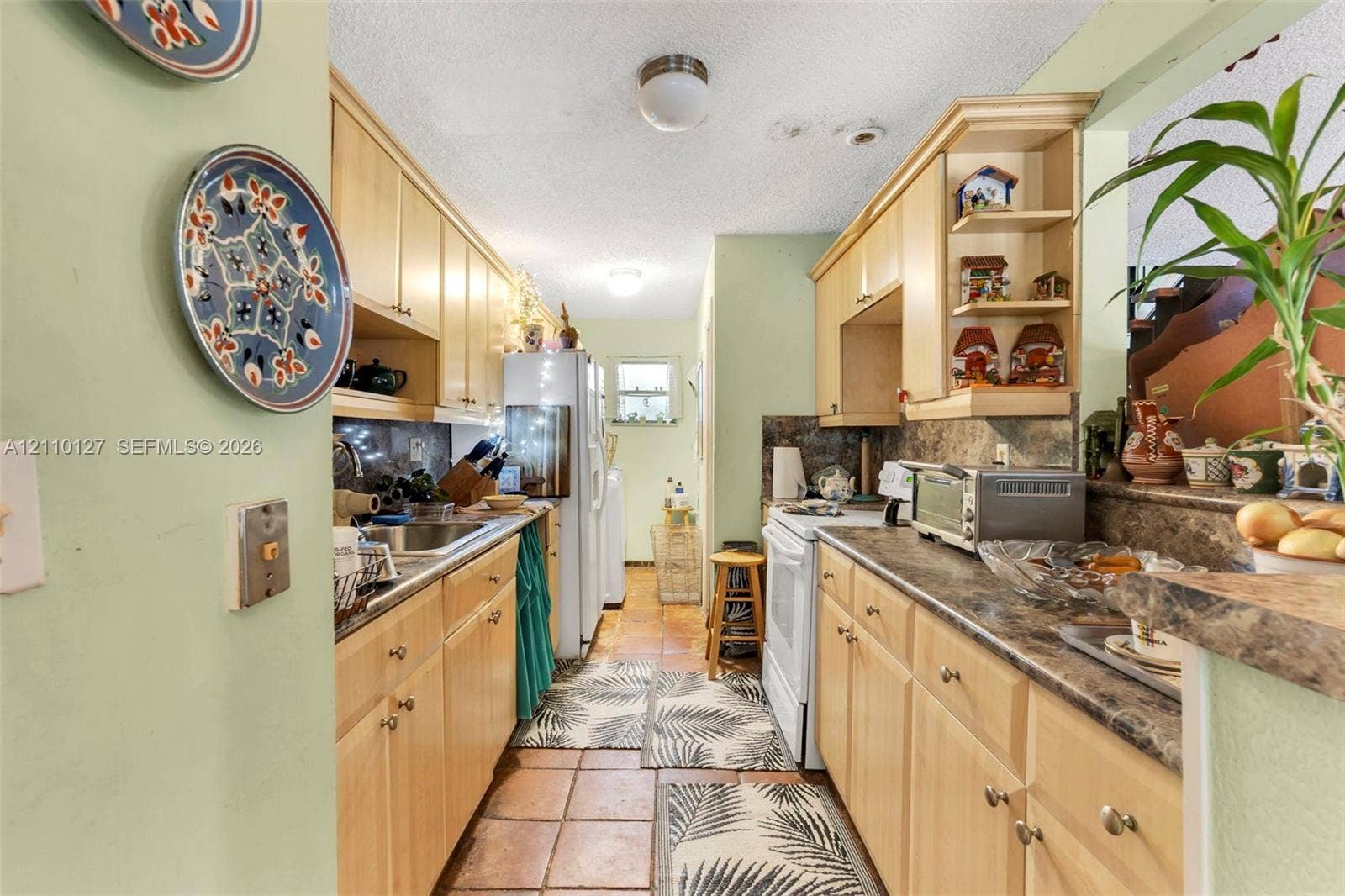 10164 SW 52nd Street, Cooper City, FL 33328 Galley-style kitchen featuring light-tone wood cabinetry, built-in open shelving, laminate countertops, and ceramic tile flooring