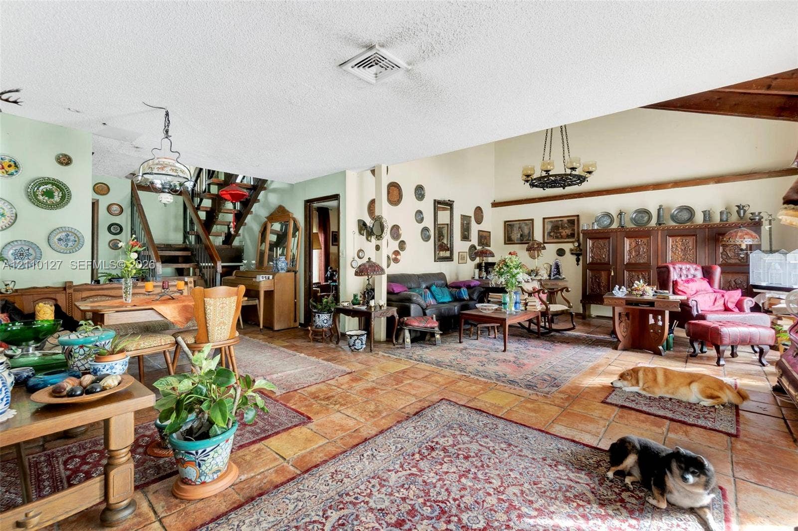 10164 SW 52nd Street, Cooper City, FL 33328 Open-concept living space featuring vaulted ceilings with exposed wood beams, terracotta tile flooring, a custom built-in dark wood cabinetry unit, and an open-tread staircase with wood handrails