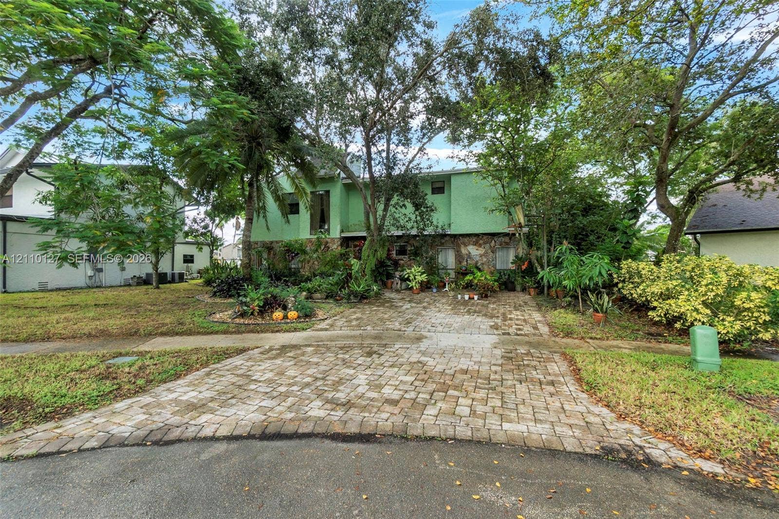 10164 SW 52nd Street, Cooper City, FL 33328 Two-story exterior featuring a stone masonry lower facade, upper-level balcony, and a multi-car paver driveway surrounded by mature landscaping