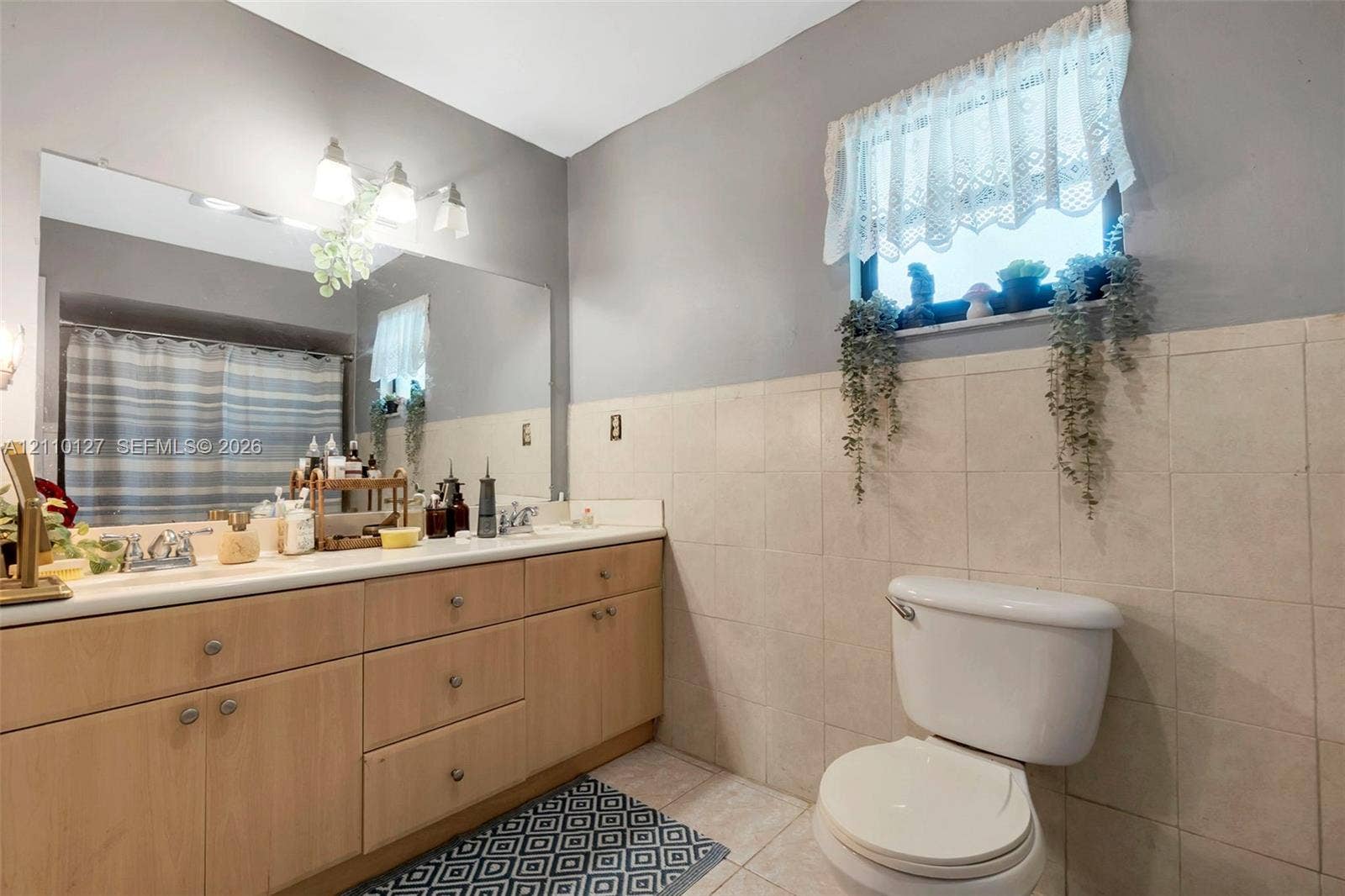 10164 SW 52nd Street, Cooper City, FL 33328 Bathroom featuring a wood-finish vanity with a light-toned countertop, large wall-mounted mirror, three-light fixture, and neutral wall tiling