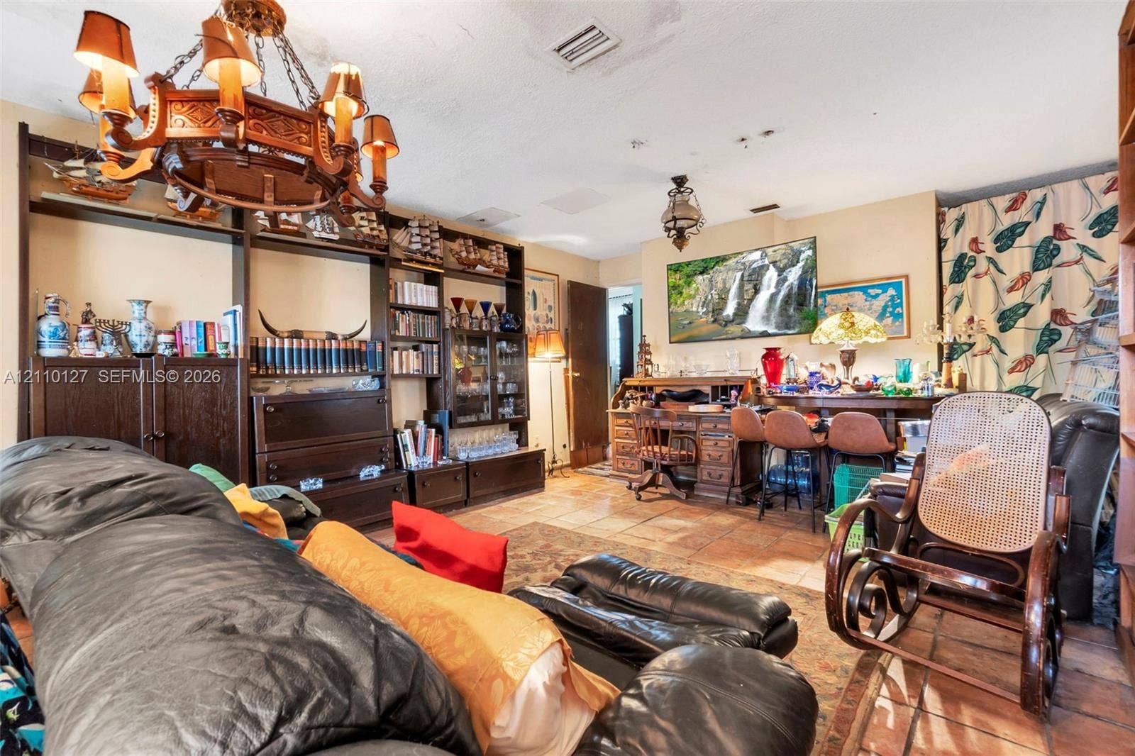 10164 SW 52nd Street, Cooper City, FL 33328 Living space featuring floor-to-ceiling dark wood built-in cabinetry, ornate metal chandelier, and terracotta-toned tile flooring